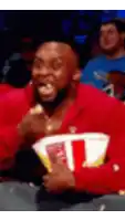 a man in a red shirt is eating popcorn while watching a basketball game