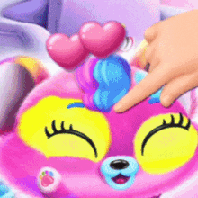 a person is touching a pink and yellow stuffed animal with hearts on its head .