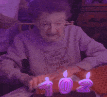 an elderly woman is crying while sitting at a table with a cake and candles with the number 103 on them
