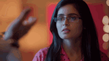 a woman wearing glasses and a pink shirt is looking at the camera