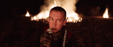 a man is holding a microphone in front of a fire with a strap that says ' ukzd ' on it