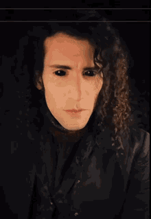 a man with long curly hair and black eyes is looking at the camera