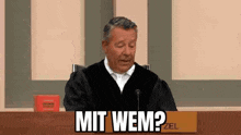 a man in a judge 's robe is sitting at a table with a sign that says `` mit wem '' .