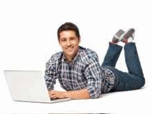 a man in a plaid shirt is laying on the floor using a laptop