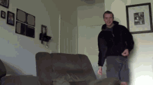 a man in a black jacket is standing in a living room with pictures on the wall