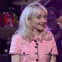 a woman with blonde hair is wearing a pink dress and smiling while sitting on a stage .