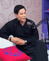 a man in a black shirt sits in front of a microphone with a bottle of water in the background