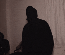 a person wearing a black hooded sweatshirt with a white curtain behind them