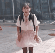 a woman wearing a pink pleated skirt and a white shirt is standing on a sidewalk