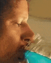 a man drinking a blue liquid from a glass