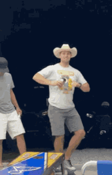 a man in a cowboy hat is dancing in front of a cornhole table .