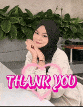 a woman in a hijab sits at a table with a pink heart and the words thank you