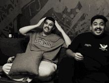 a man wearing a question mark shirt sits next to a man wearing a black shirt