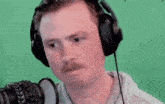 a man wearing headphones and a mustache is laughing in front of a green screen .