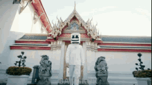 a man wearing a marshmello mask stands in front of a building in bangkok