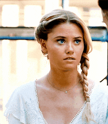 a woman wearing a braided ponytail and a necklace looks at the camera