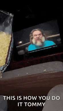 a man with a beard is sitting in front of a television watching a show .