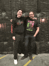 a man wearing a shirt that says so tell me what do you fear stands next to another man