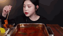 a woman is sitting at a table eating a skewer of food .