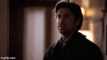 a man in a black jacket is standing in a hallway looking at something .
