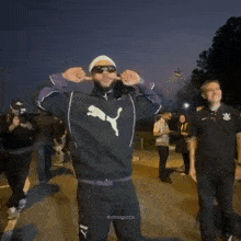a man wearing sunglasses and a puma sweatshirt is standing in front of a crowd