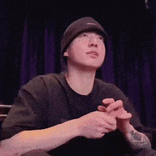a man wearing a beanie and a black shirt is sitting on a stage .