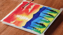 a painting of a sunset with trees and mountains on a wooden table
