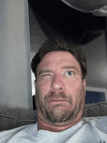 a man with a beard is making a funny face with one eye closed