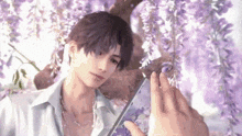 a man is taking a picture of himself with a cell phone while standing under a tree with purple flowers .