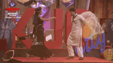 a man and woman are dancing in front of a bigg boss banner