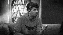 a man is sitting on a couch wearing a sweatshirt that says the ultimate