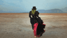 a woman wearing a black hat and a red skirt is walking in the desert
