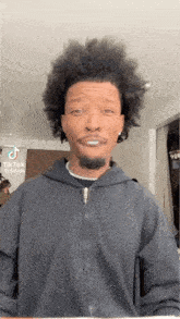 a man with curly hair and a beard is making a funny face while wearing a black hoodie .
