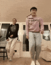 two people are dancing in a living room and one of them is wearing a pink sweatshirt that says reebok on it