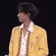 a young man in a yellow jacket and white shirt is standing on a stage .