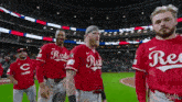 a group of reds baseball players are standing on the field .