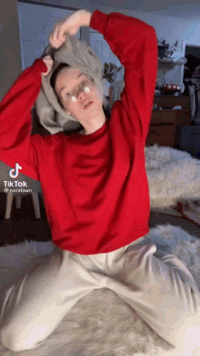 a woman wearing a red sweater and white pants is kneeling down on a bed .