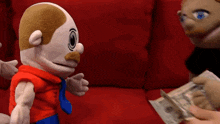 two stuffed animals are sitting on a red couch while a person holds a bunch of money in front of them