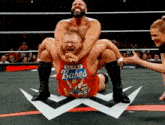 a wrestler wearing a red shirt that says babes is being lifted by another wrestler