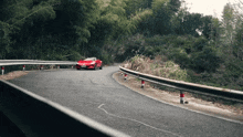 a red car is driving down a curvy road with trees in the background