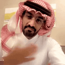 a man with a beard and glasses is wearing a keffiyeh and a head scarf .
