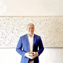 a man in a blue suit is standing in front of a white wall