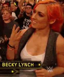 a woman with red hair is standing in front of a crowd while wearing a white tank top and a black vest .