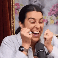 a woman is laughing in front of a microphone while wearing an apple watch and a ring .
