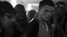 a black and white photo of a man standing in a crowd of people at a party .