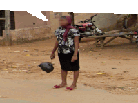 a woman standing in a dirt area with a sign on the wall that says " no parking "