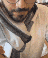 a man with glasses and a scarf around his neck looks at his phone