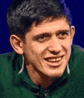 a man wearing a green jacket is smiling with a blue background
