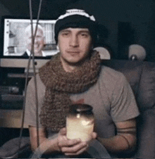 a man wearing a scarf and a hat is holding a jar of honey .