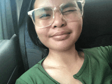 a woman wearing glasses and a green shirt winks at the camera